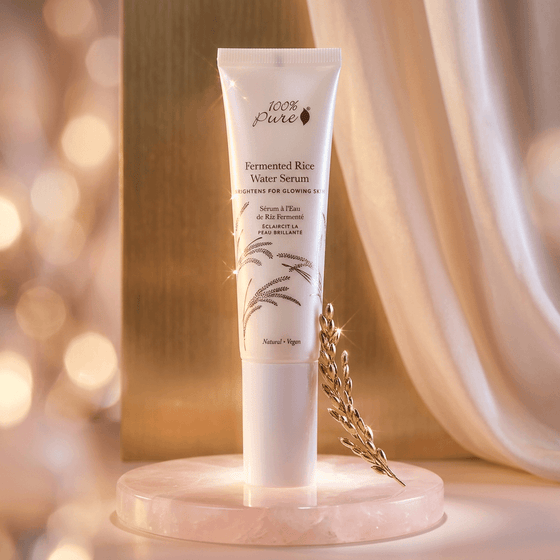 Tube of 100% Pure Fermented Rice Water Serum on a decorative stand with a soft, blurred background.