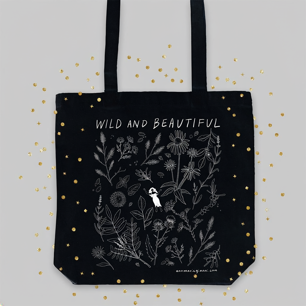 Black tote bag with floral design and 'Wild and Beautiful' text on a light gray background with gold dots.