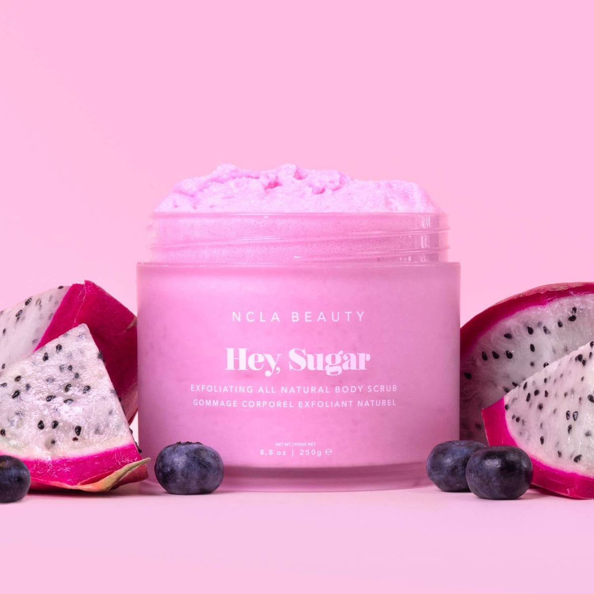 Pink body scrub container with dragon fruit and blueberries on a pink background