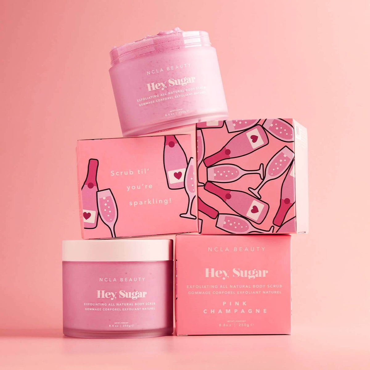 Pink skincare products with 'Hey Sugar' and 'Pink Champagne' packaging on a pink background