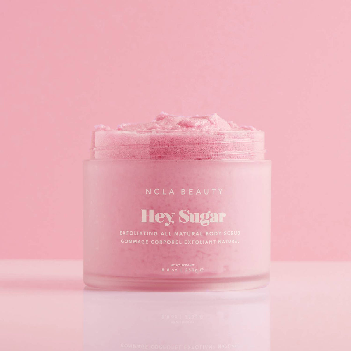 Pink jar of NCLA Beauty 'Hey, Sugar' exfoliating body cream on a pink background