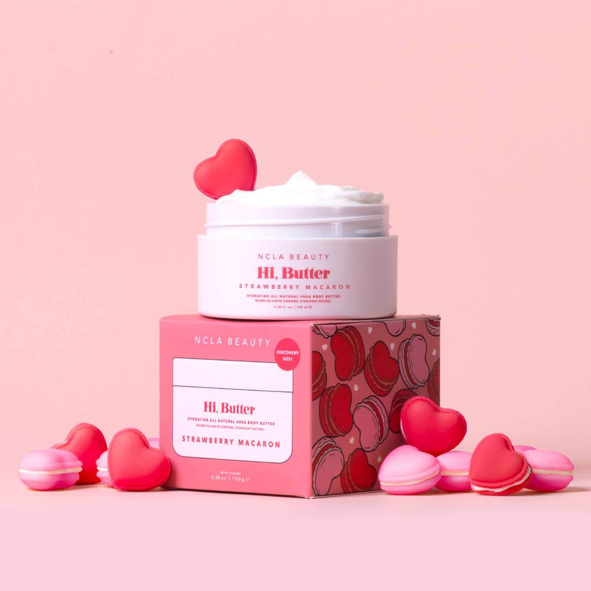 NCLA Beauty HI Butter Strawberry Macaron product with pink packaging and heart-shaped decorations on a pink background