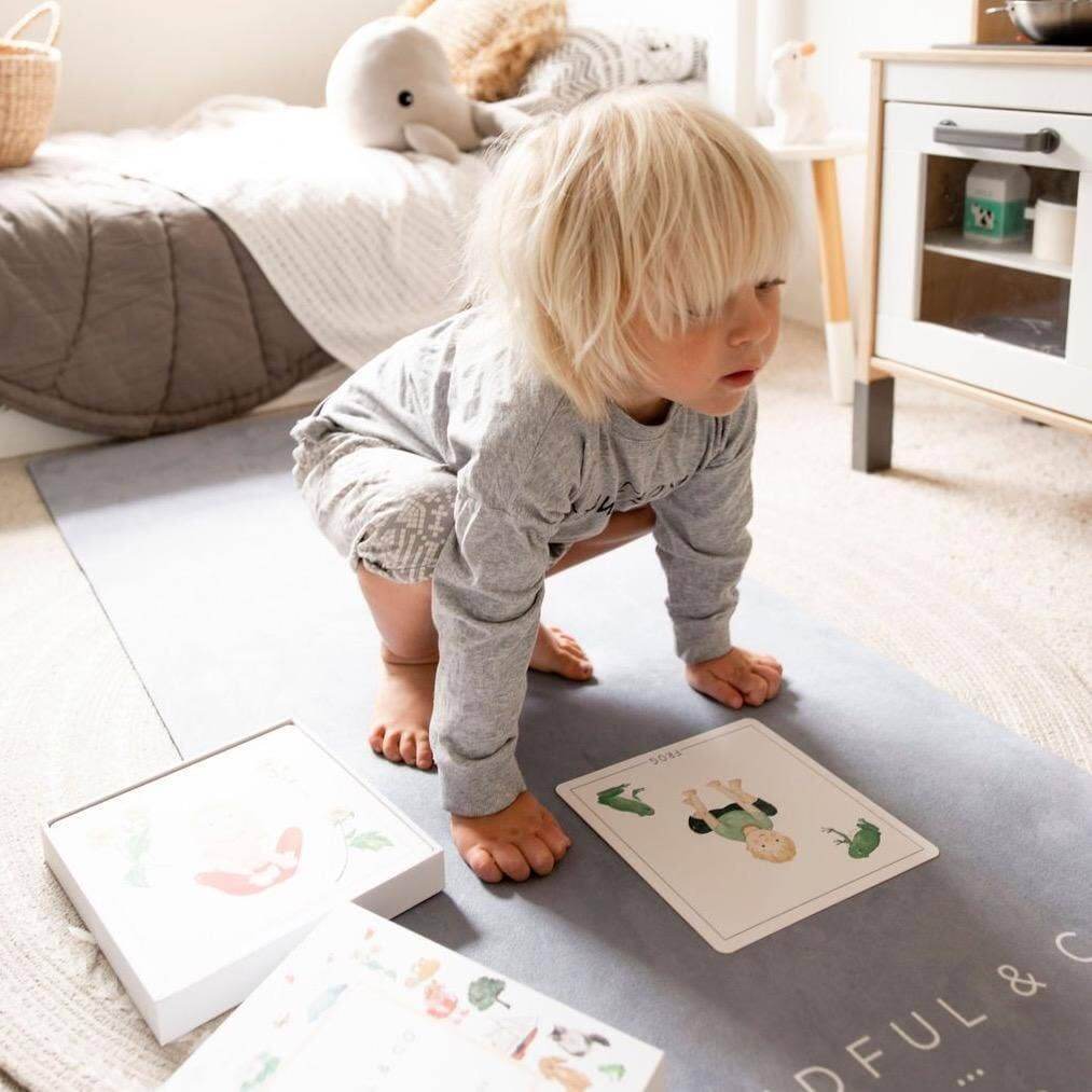 Child playing with educational cards on a mat in a room with toys and furniture.