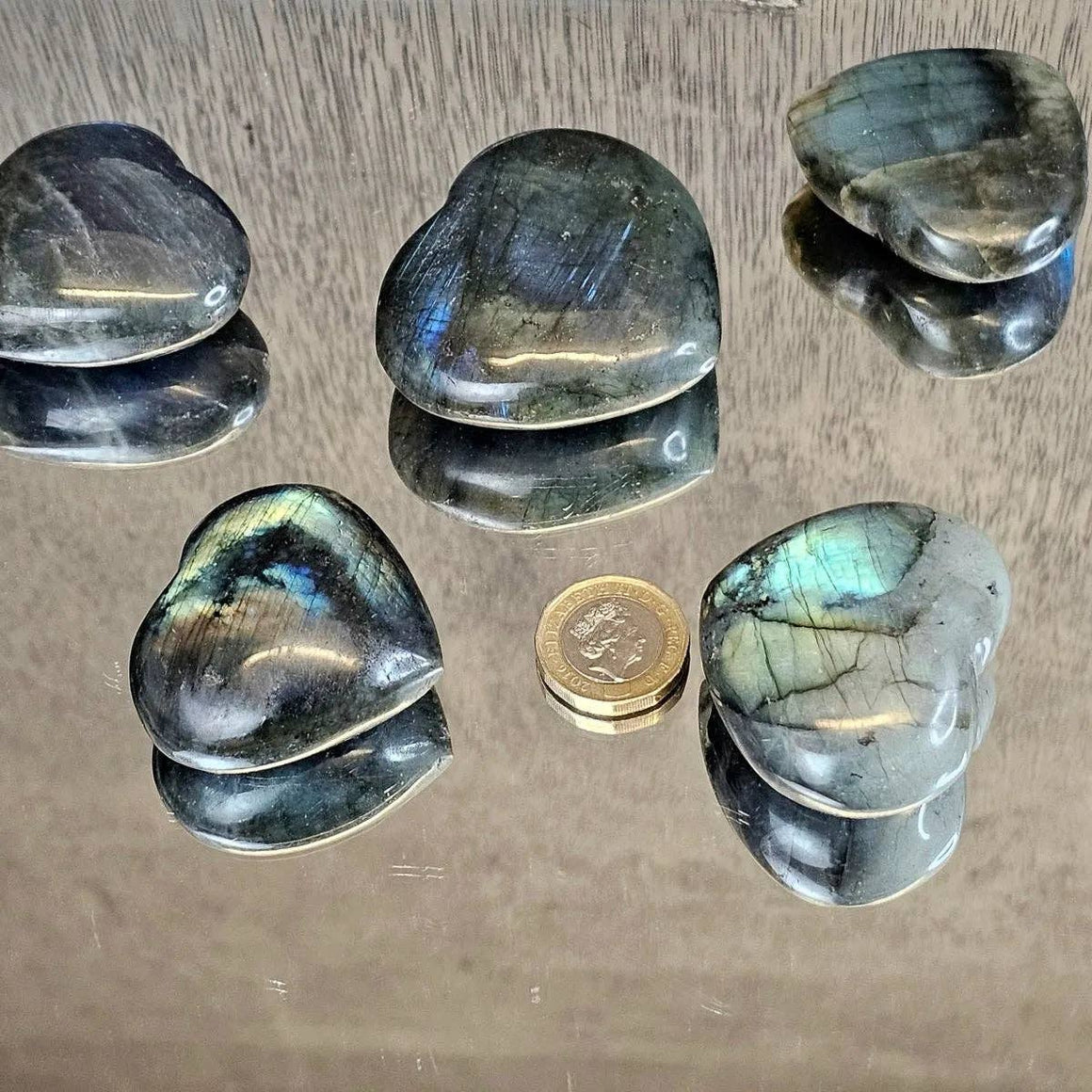 Five Labradorite stones on a reflective surface with a coin for scale.