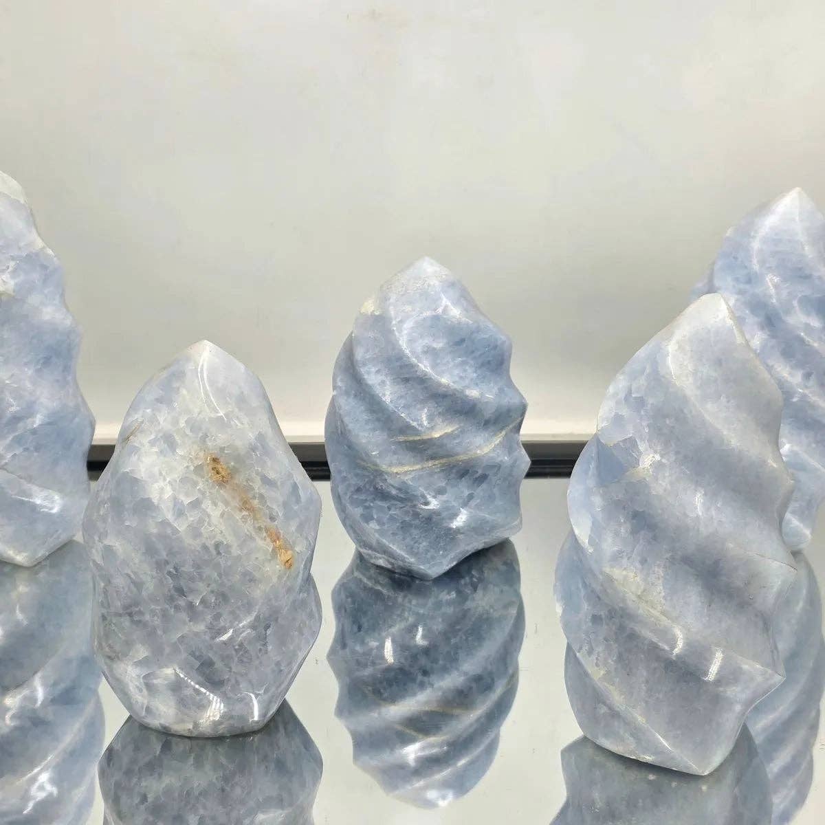 Group of blue calcite crystals on a reflective surface with a white background