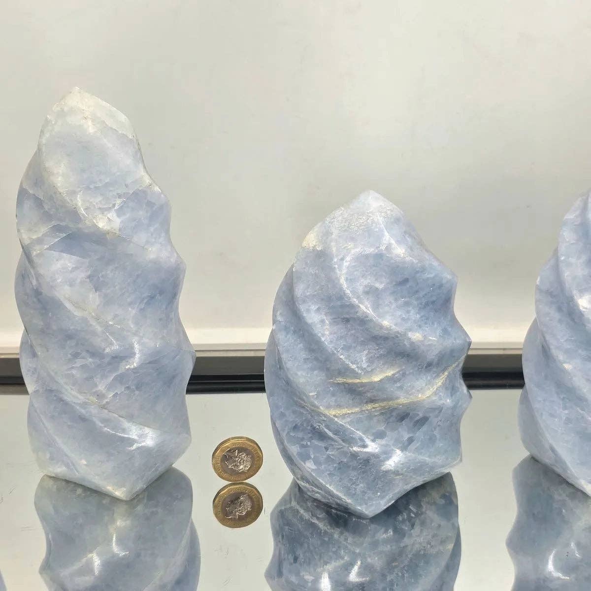 Three blue crystal formations with a coin for scale on a reflective surface.