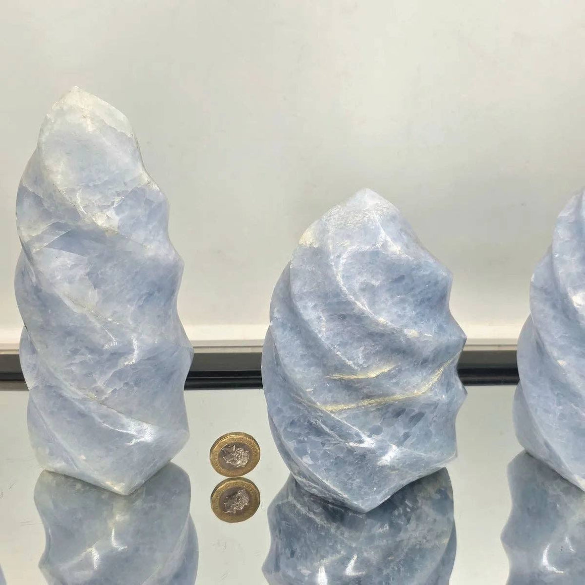 Three blue crystal formations with a coin for scale on a reflective surface.