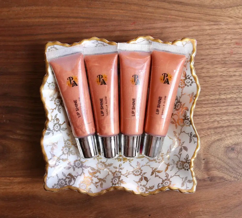 Four lip gloss tubes on a decorative tray with a wooden background