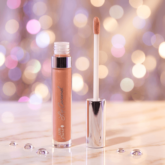 Lip gloss with applicator on a reflective surface against a bokeh light background
