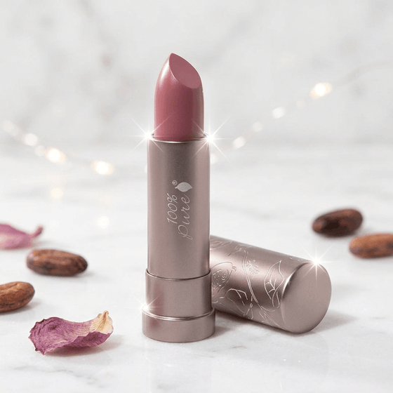 Lipstick with a brand logo on a light background with almonds and petals