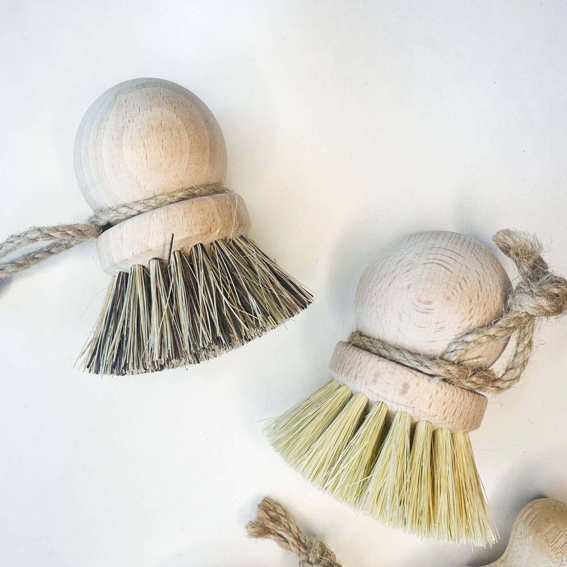Two wooden ball tassels with natural fibers on a white background