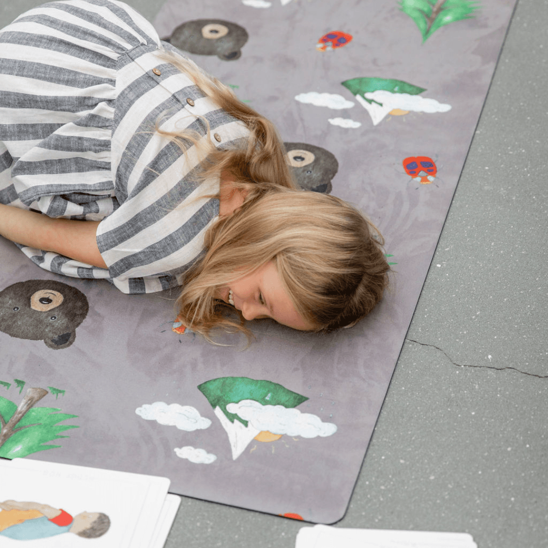 Child practicing on a Nature Print Kids Yoga Mat featuring playful animal and nature illustrations.