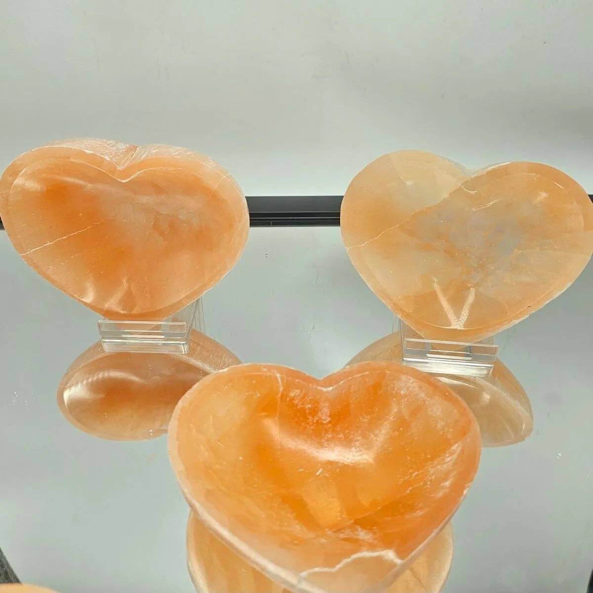 Three heart-shaped orange stones on clear stands against a light gray background