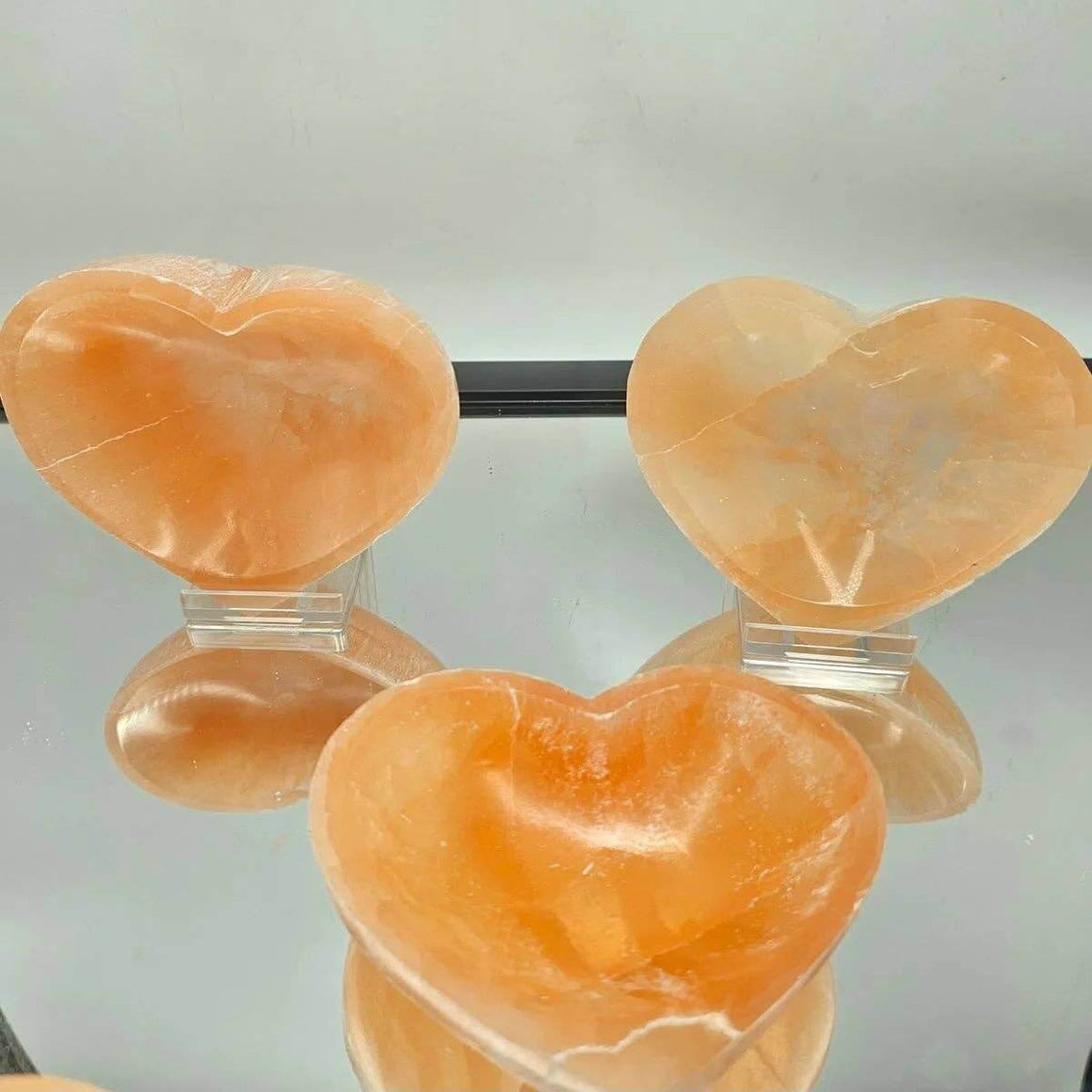 Three heart-shaped orange stones on clear stands against a light gray background