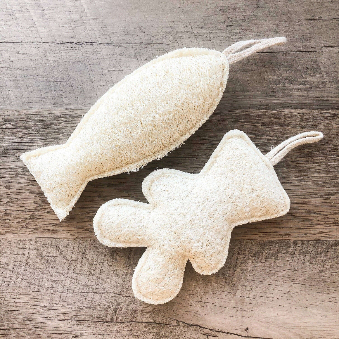 Two textured, beige bath pouf toys on a wooden surface