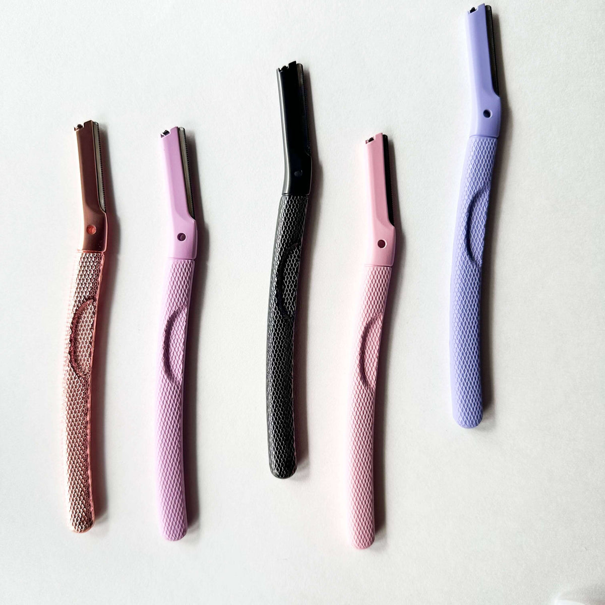 Five eyebrow razors of different colors on a white background
