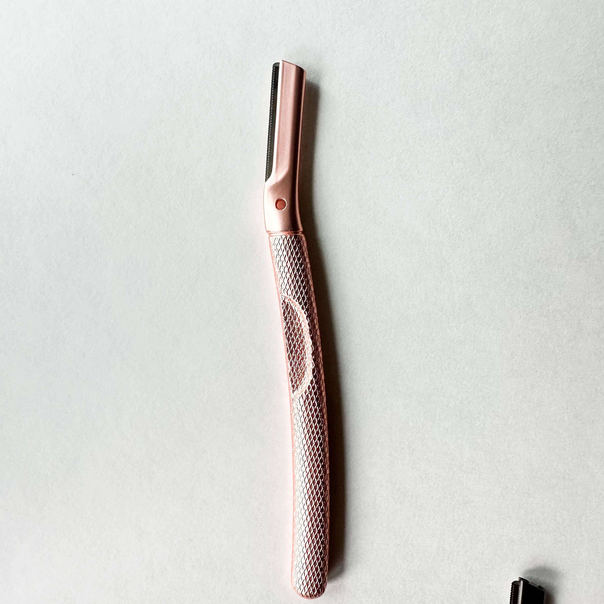 Rose gold eyebrow razor on a light gray background