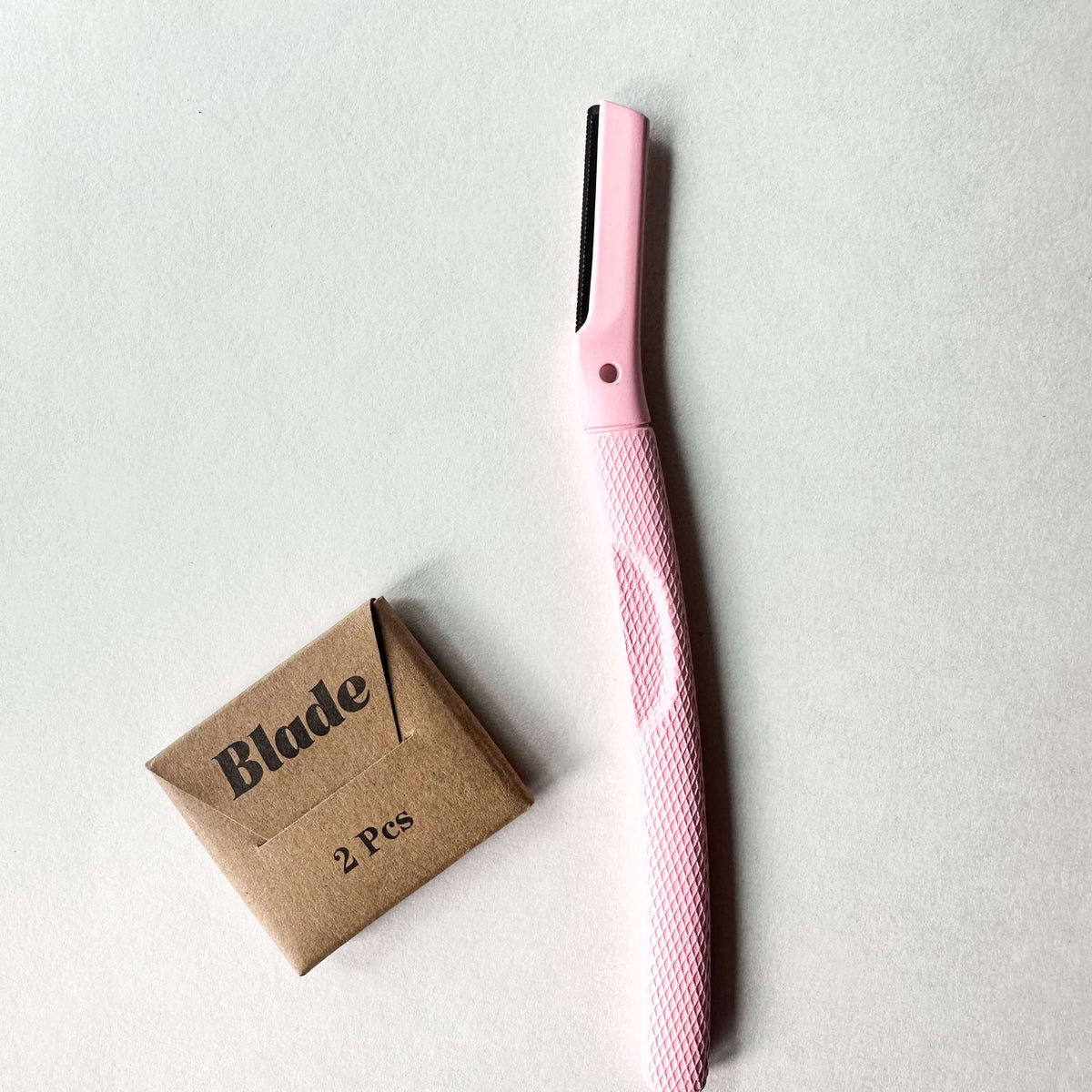 Pink razor with a cardboard packaging labeled 'Blade 2 Pcs' on a light gray background