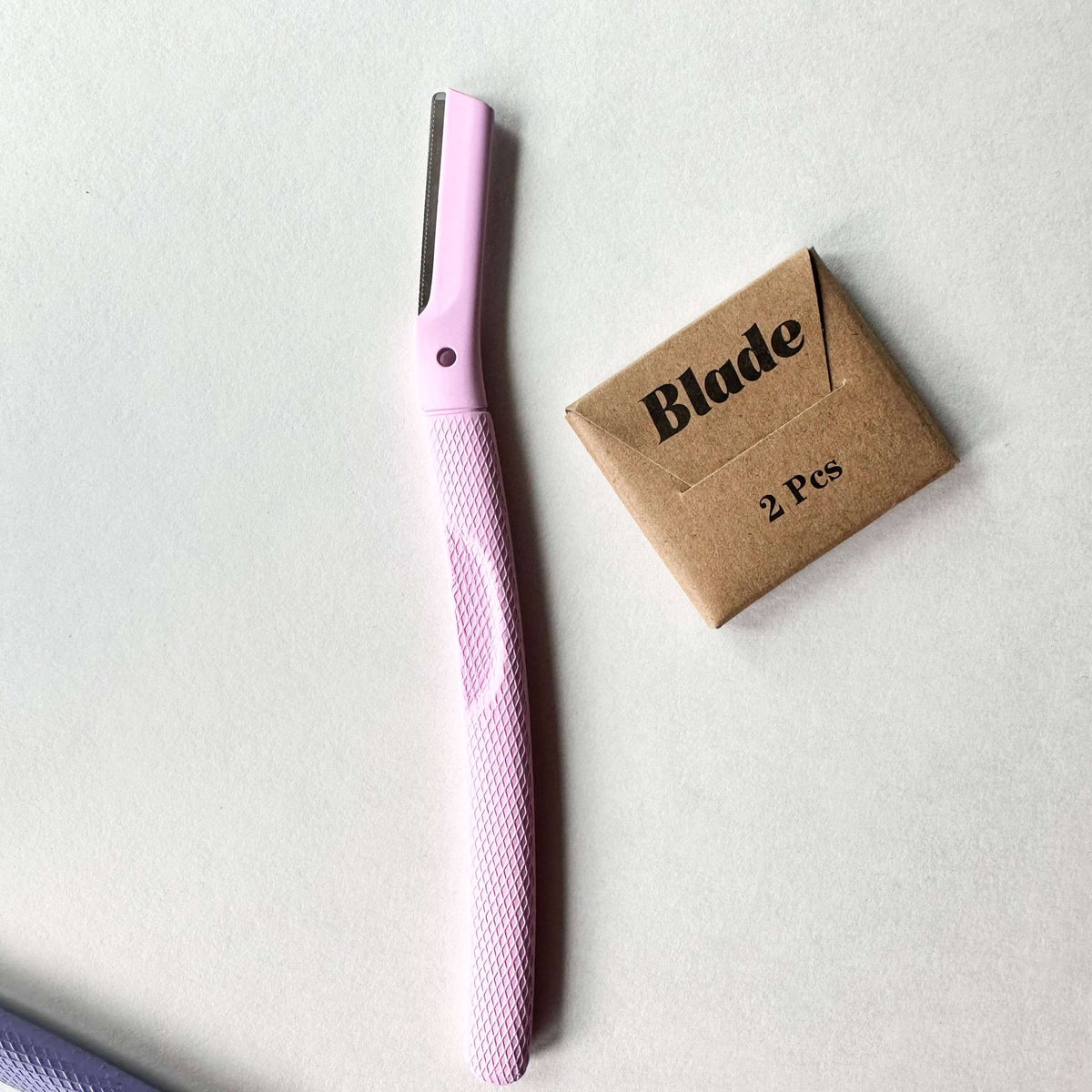 Pink hair straightener with a cardboard box labeled 'Blade 2 Pcs' on a light gray background