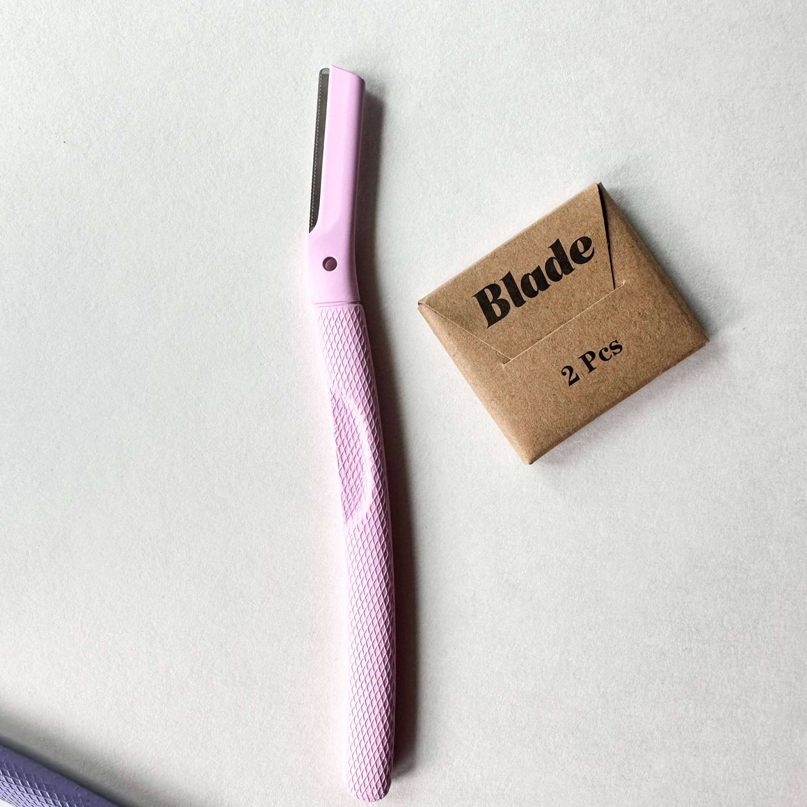 Pink hair straightener with a cardboard box labeled 'Blade 2 Pcs' on a light gray background