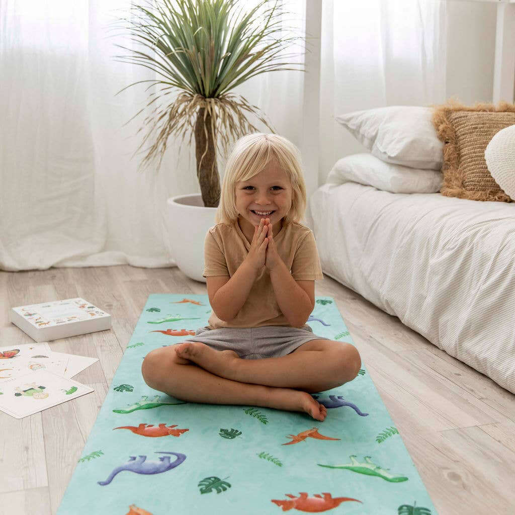 Child sitting on a colorful dinosaur mat in a bright room with a plant and white furniture.
