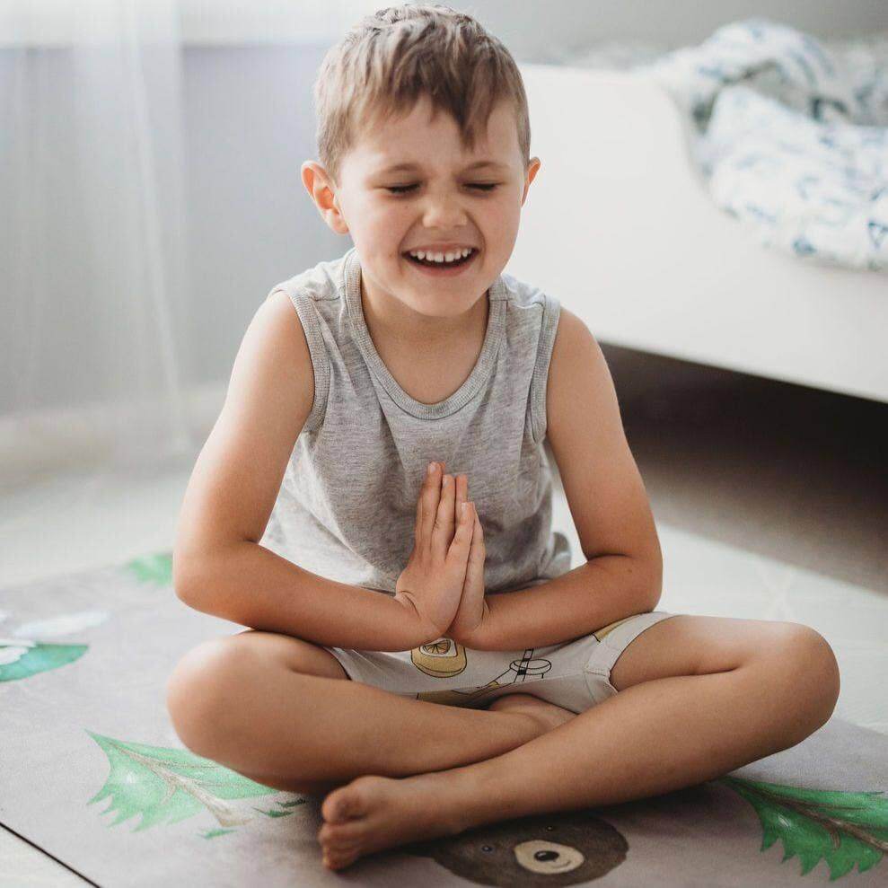 Child sitting on a play mat with hands pressed together in a room.