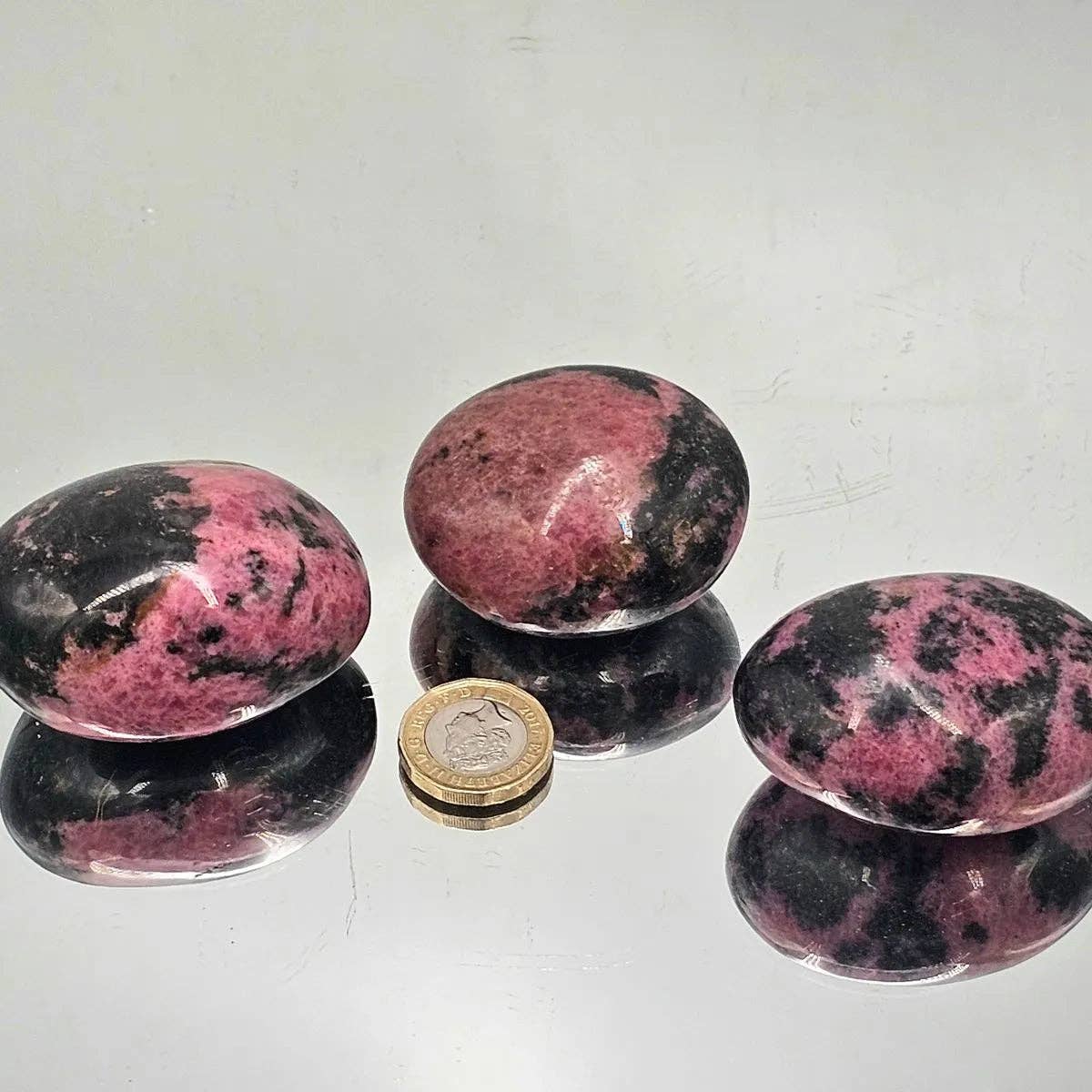 Rhodonite Crystal Palm stones displayed beside a coin, showcasing their polished surface and vibrant colors.