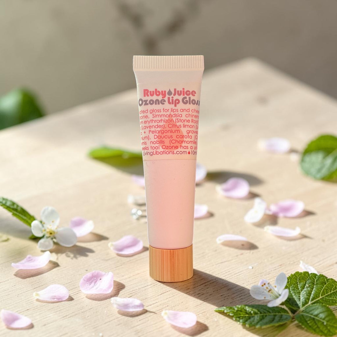 Tube of Ruby Juice lip gloss on a wooden surface with flowers and leaves