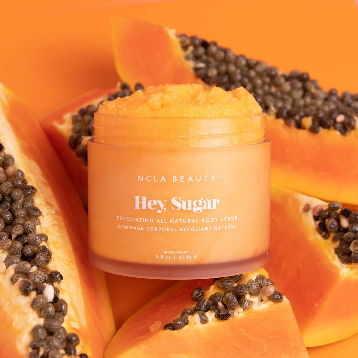 NCLA Beauty 'Hey Sugar' body scrub jar on a background of papaya slices.