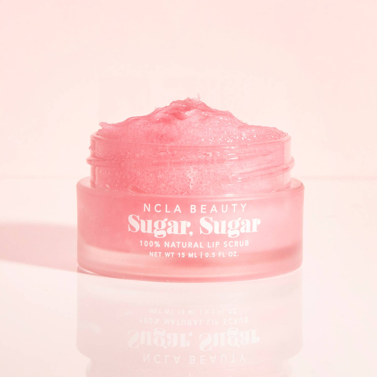 Pink lip scrub jar with 'NCLA Beauty' branding on a light pink background