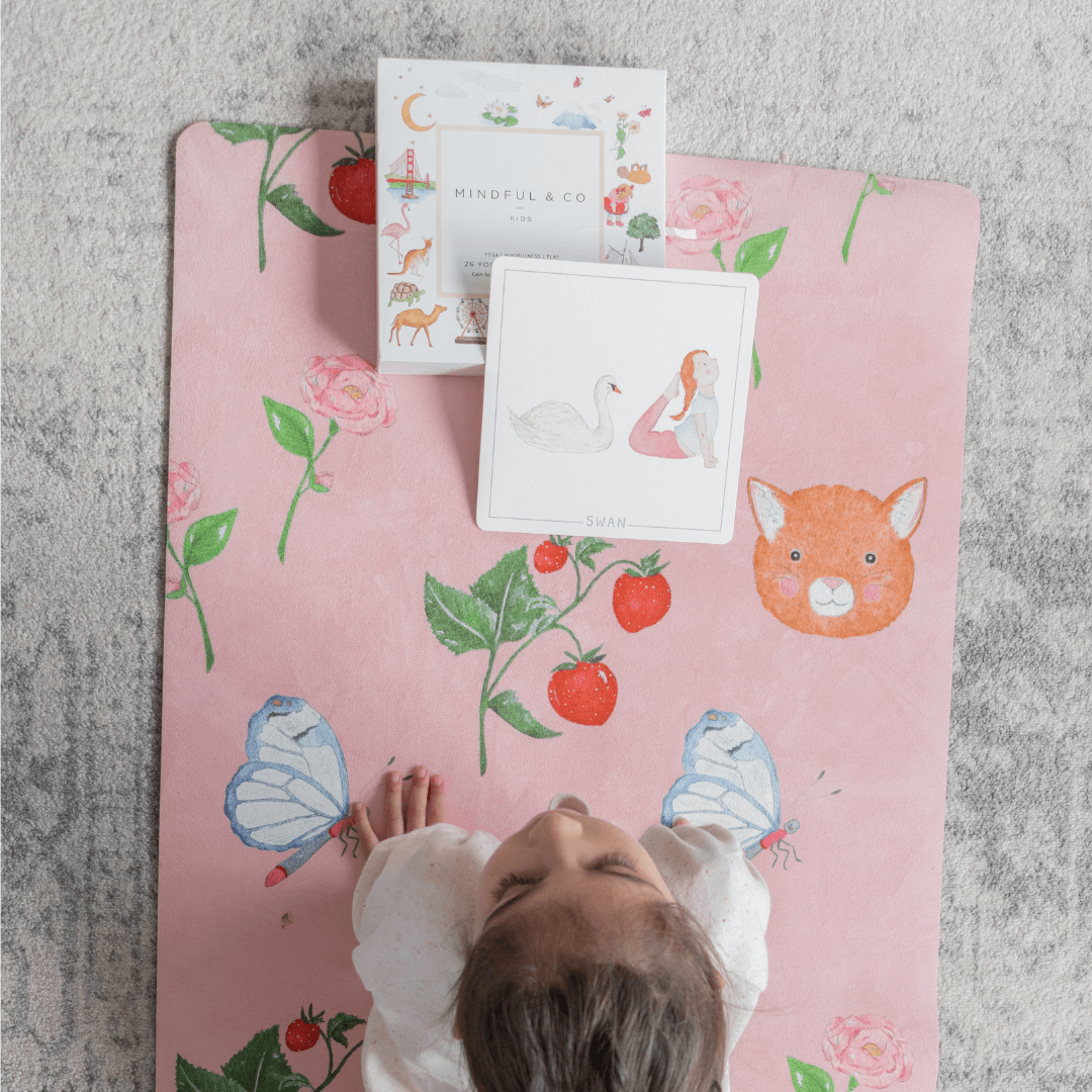 Child lying on a pink play mat with animal and nature designs, surrounded by cards.