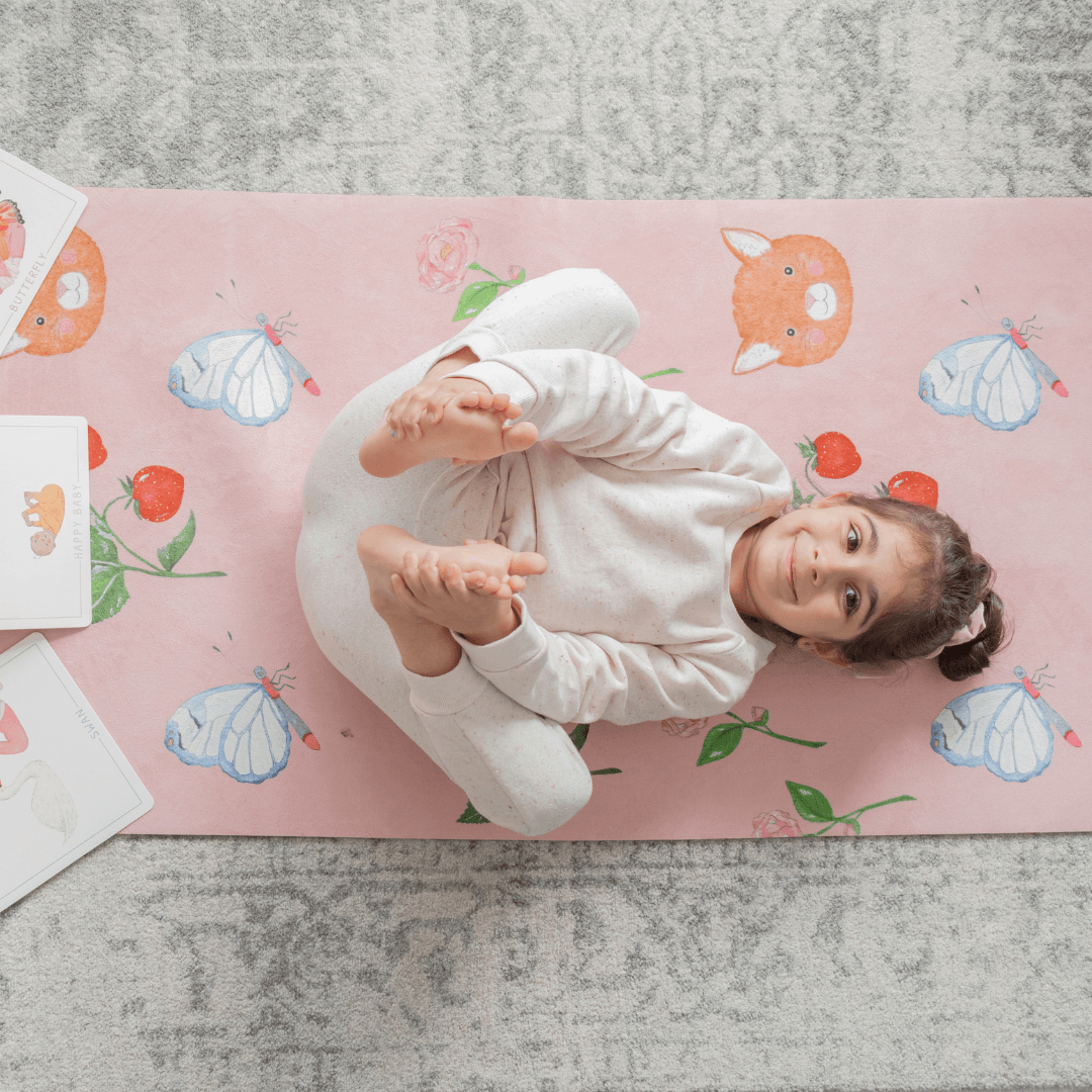 Child lying on a pink mat with cartoon designs on a gray floor.