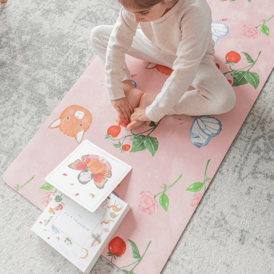 Child playing on a pink mat with animal illustrations, accompanied by children's books.