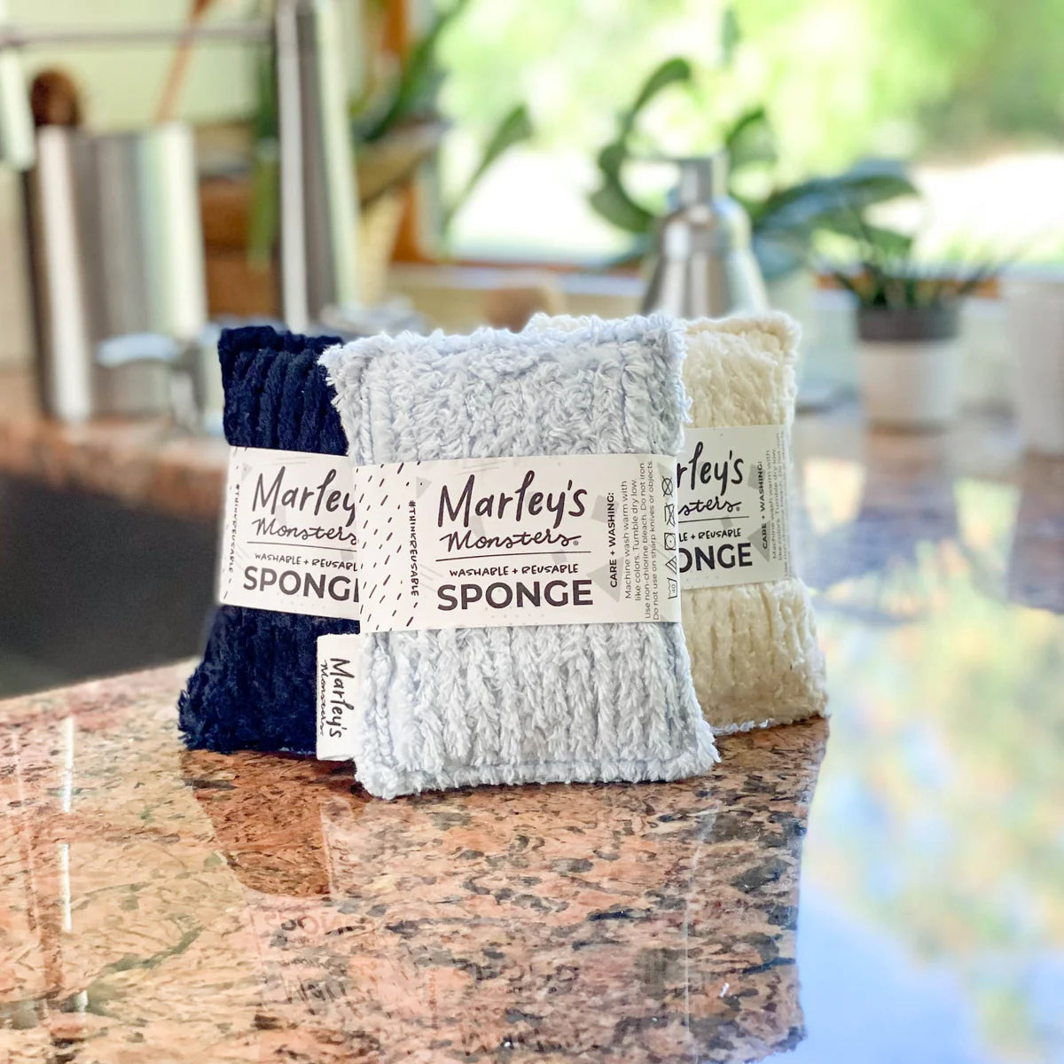 Three sponges with labels on a marble surface, blurred background of a kitchen.