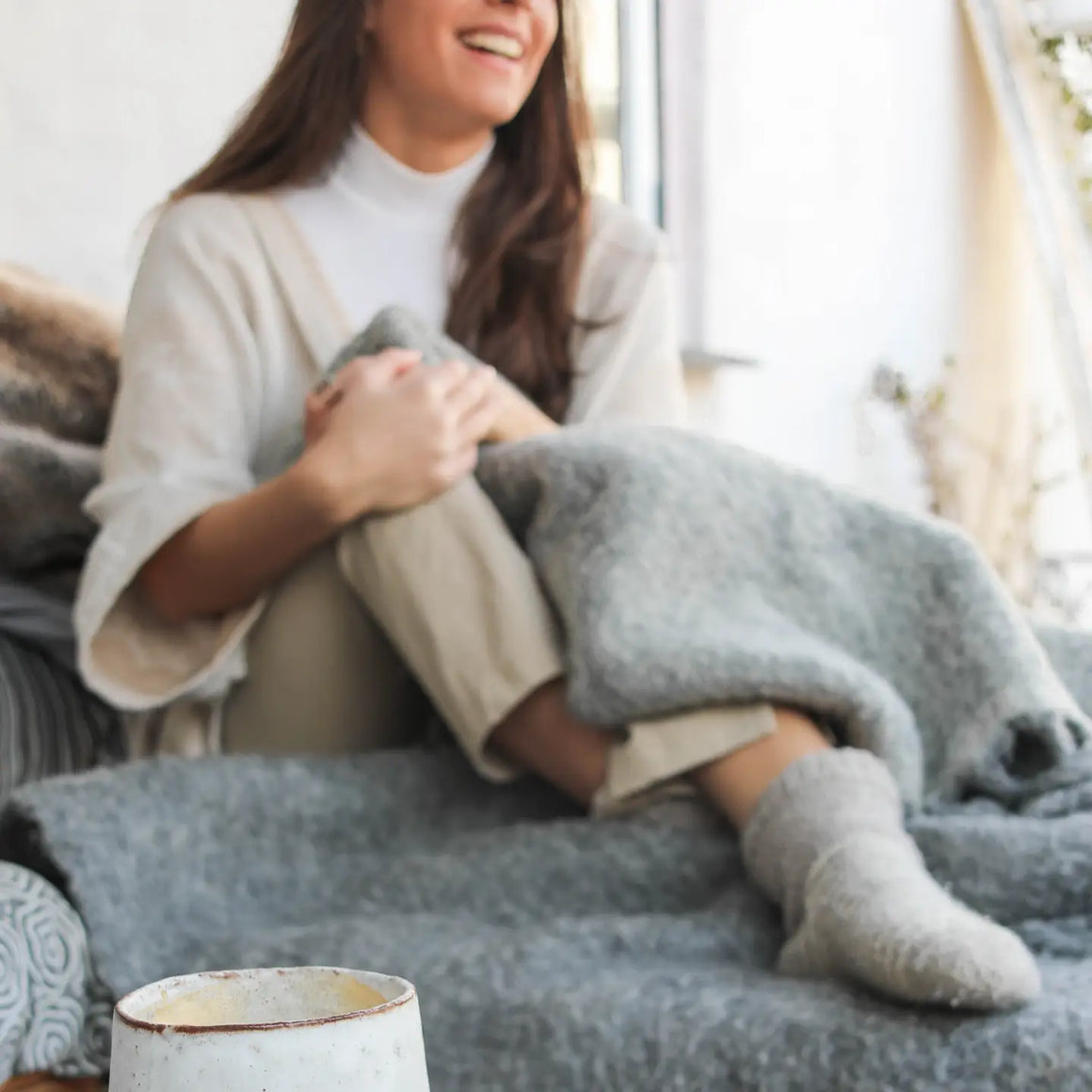 Woman wrapped in a blanket enjoying a cozy moment with a cup of Maitake Mushroom Coffee.