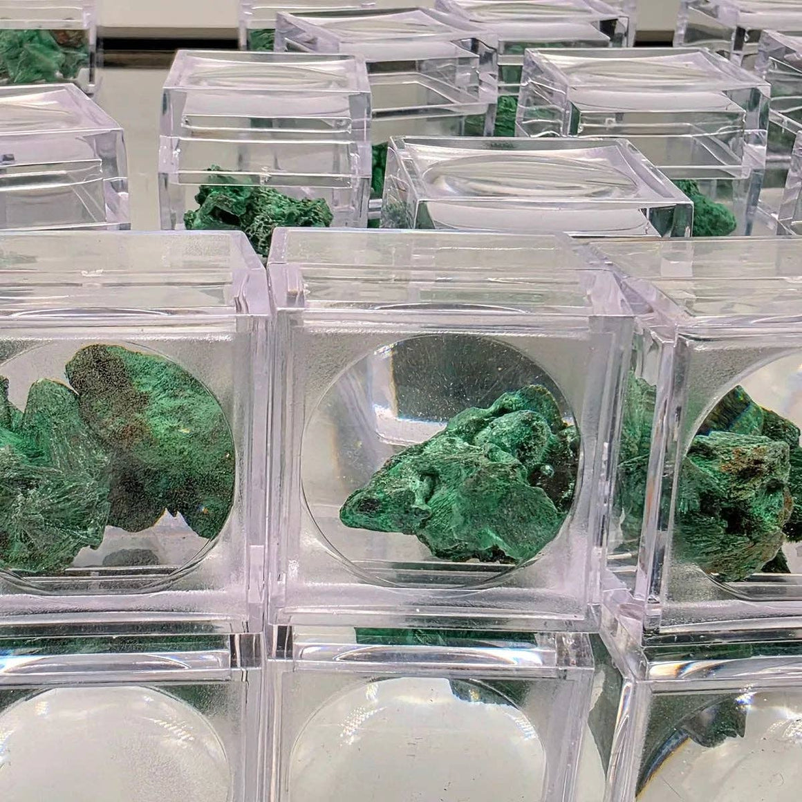 Green mineral specimens in clear acrylic cases on a grid.