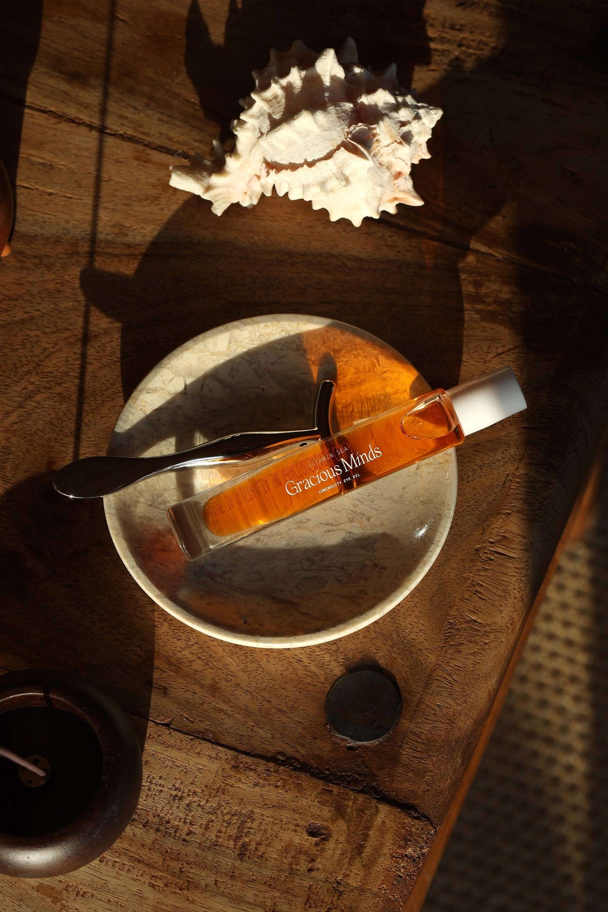 Vitamin C overnight eye oil on a marble dish with a spoon and seashells, perfect for nighttime skincare.