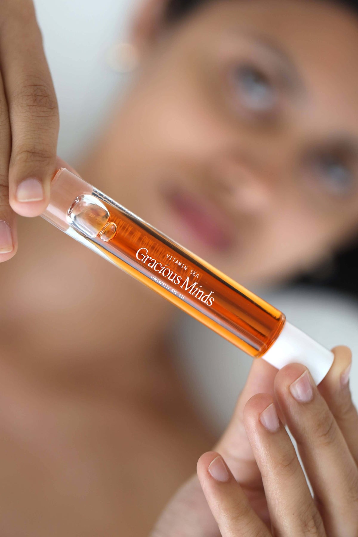 Vitamin C overnight eye oil in a clear tube held by a person, showcasing its rich orange color and luxurious design.