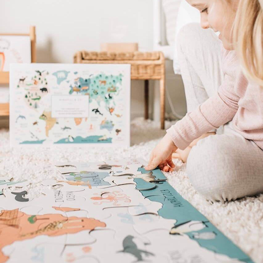 Child playing with a puzzle on a rug in a room with a bookshelf and toys.