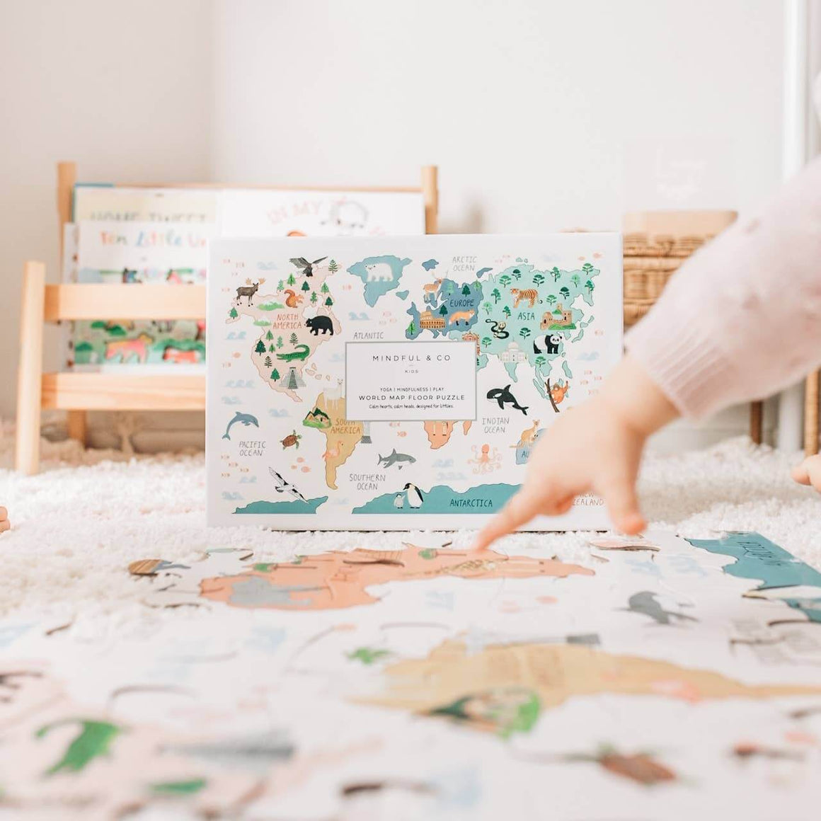 Child's hand reaching towards a world map cloth puzzle on a bed