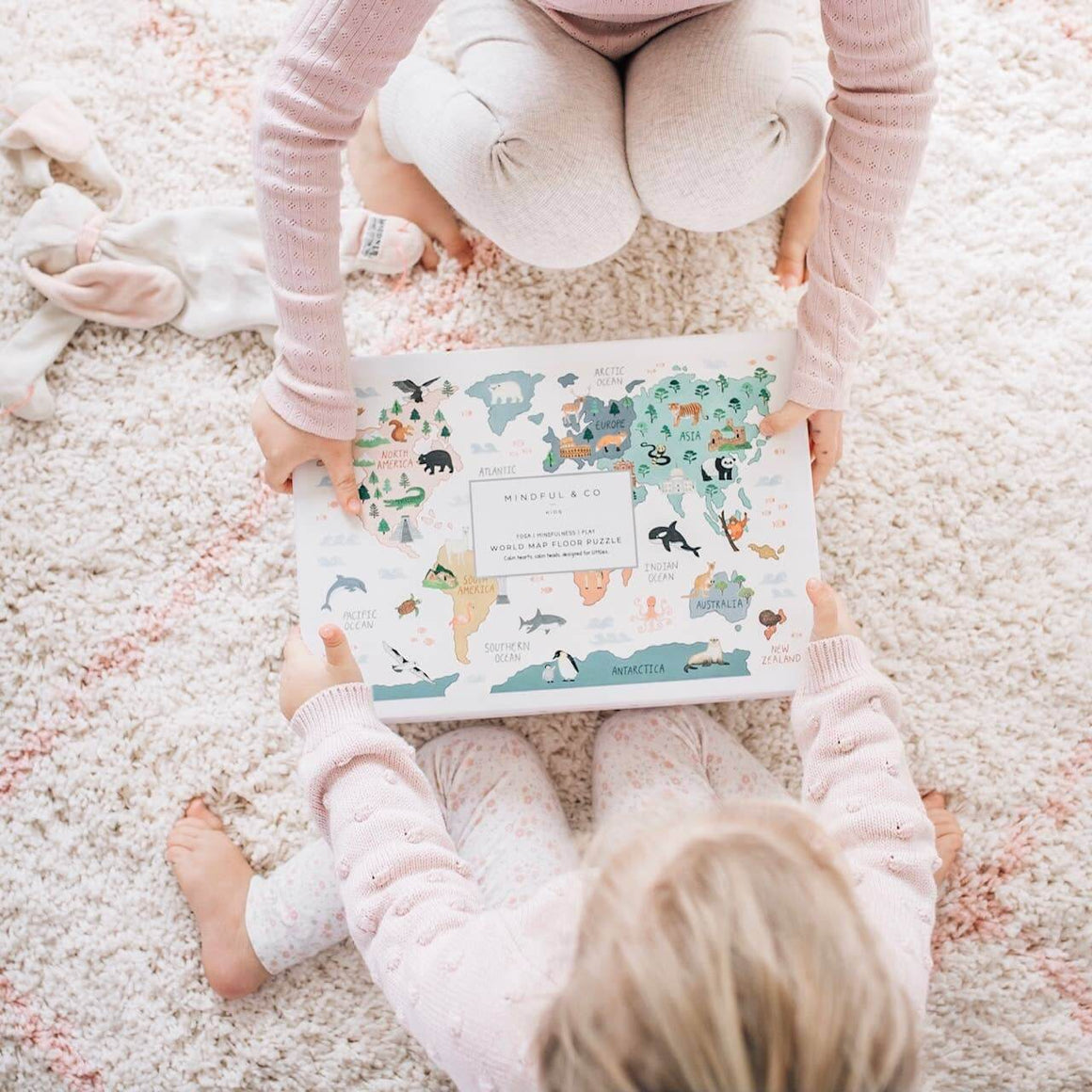 Two children sitting on a carpeted floor holding a colorful book with animal illustrations.