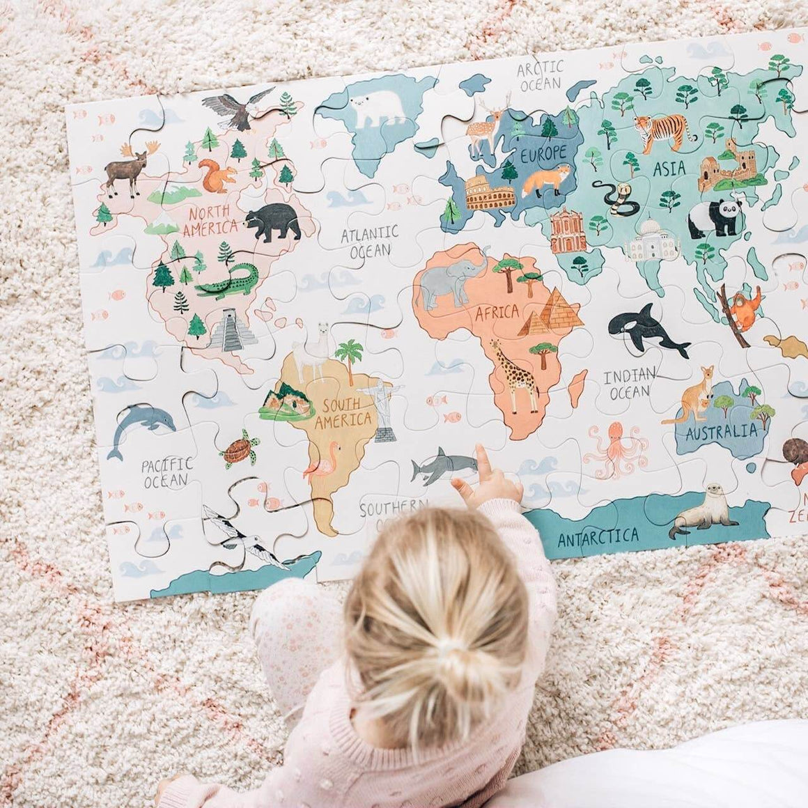 Child playing with a world map puzzle on a carpeted floor