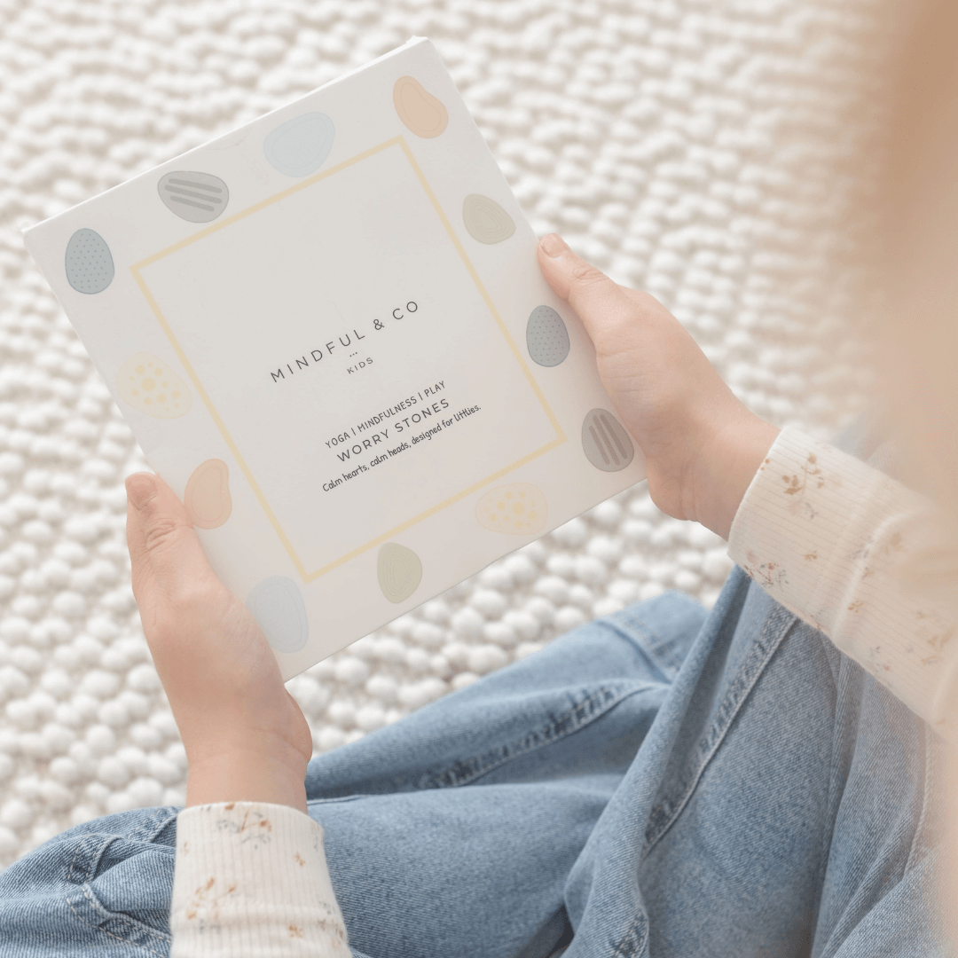 Child holding a box of Worry Stones – Calming Sensory Fidget for Kids (Set of 6) on a textured mat.