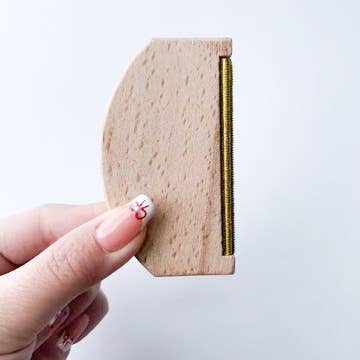 Hand holding a Plastic-Free Travel Lint Remover with a natural wooden handle and metal edge.