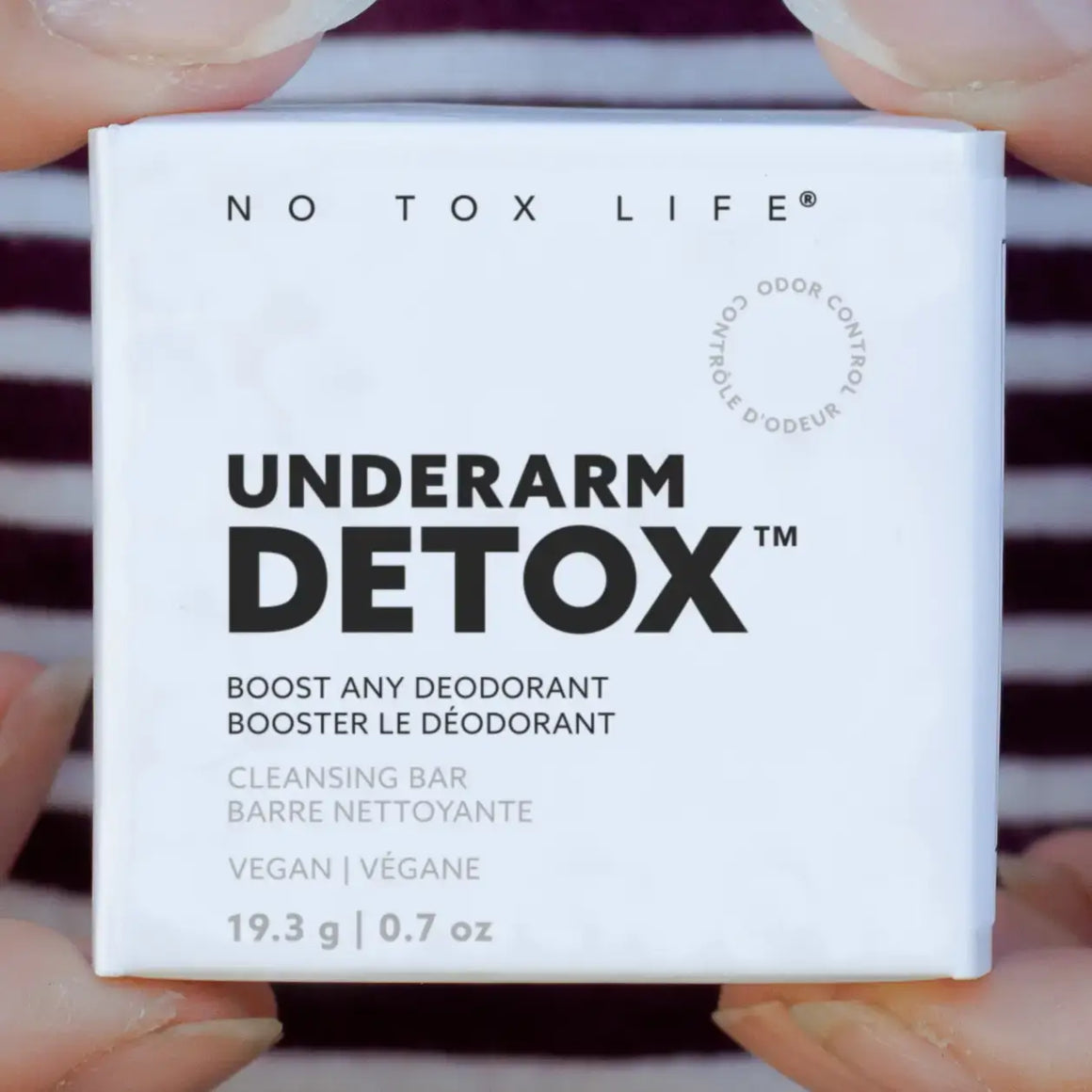 No Tox Life Underarm Detox product packaging held by hands against a blurred background