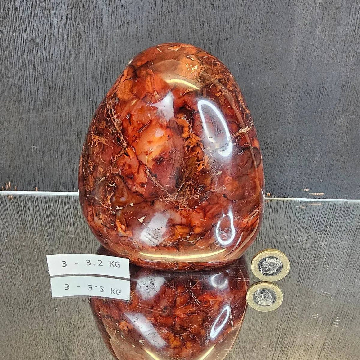Large amber stone with visible inclusions on a reflective surface, with weight labels and coins for scale.