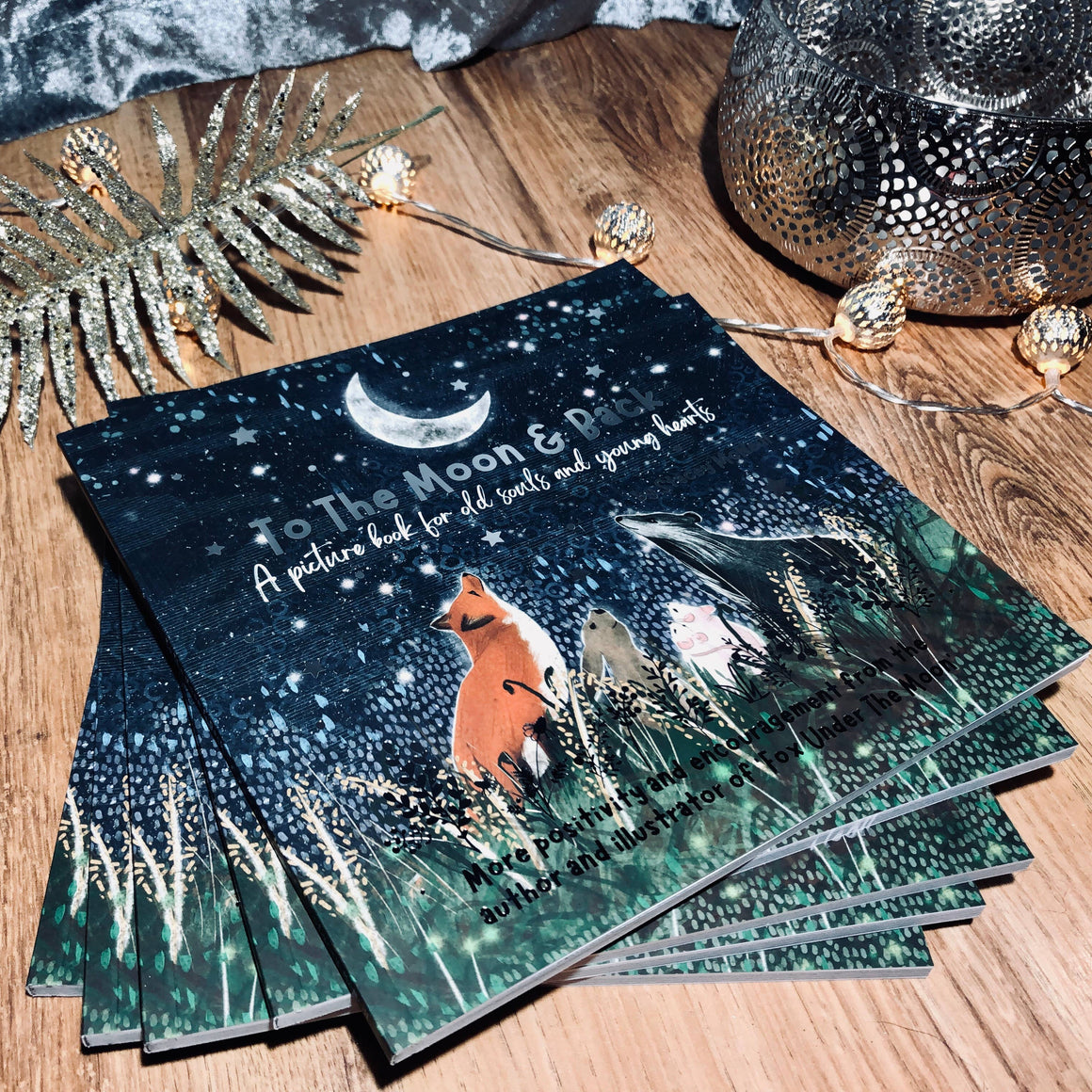 Stack of books titled 'To the Moon & Back' on a wooden surface with decorative elements.