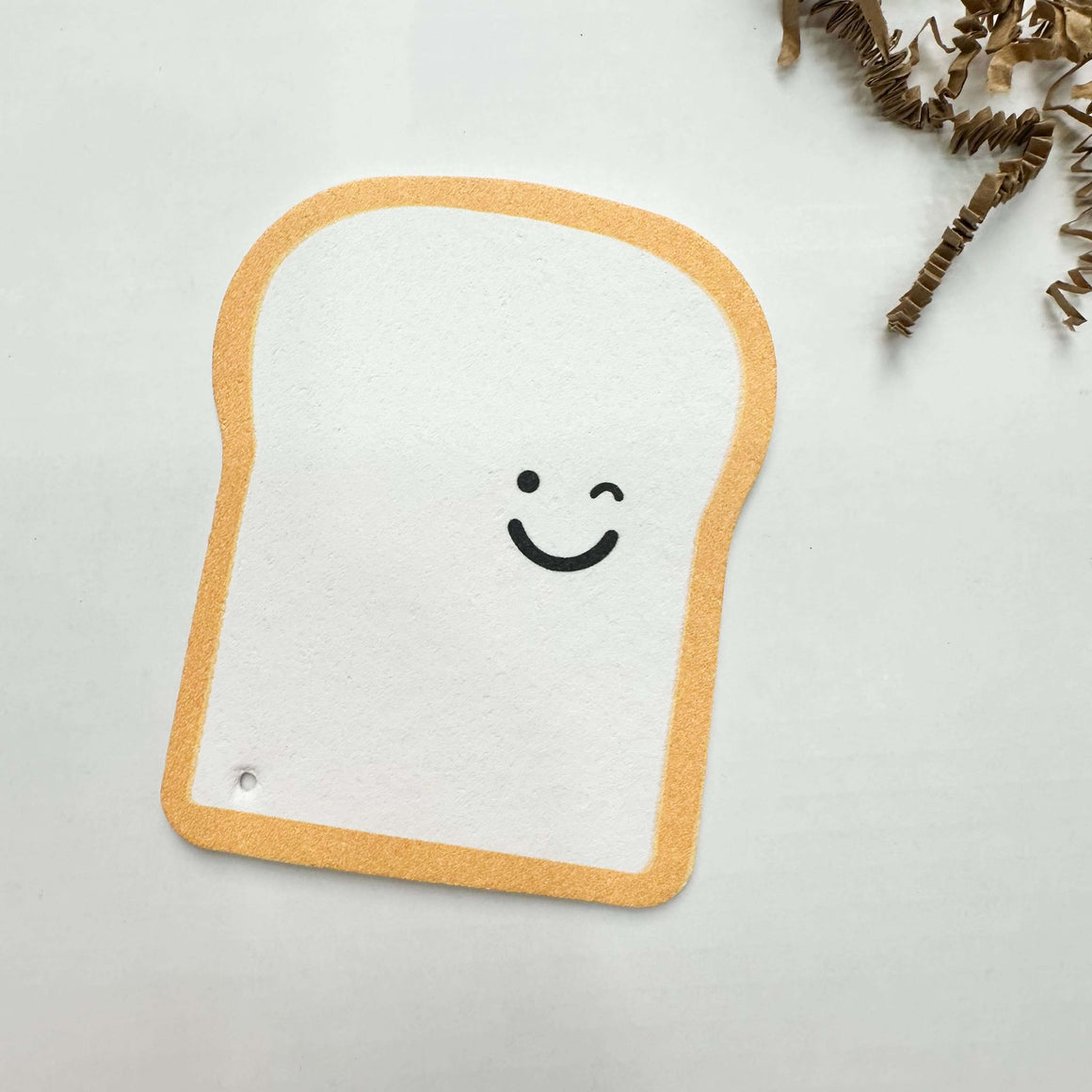 Toy resembling a slice of bread with a smiley face on a light gray background