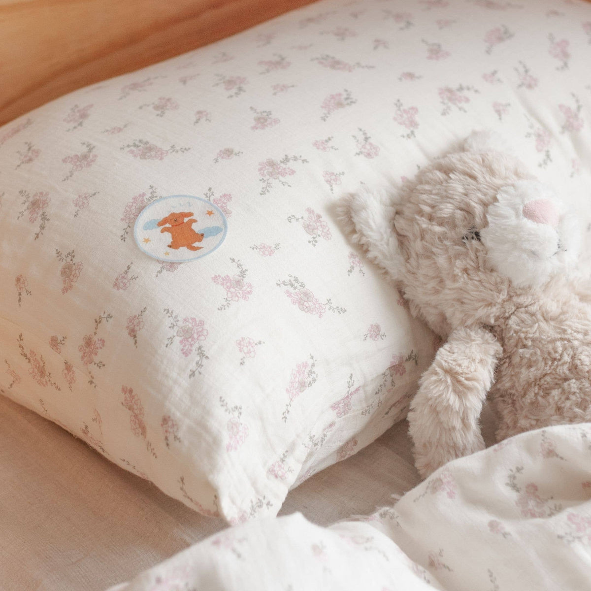 Floral-patterned pillow with a teddy bear and cartoon character on a bed.