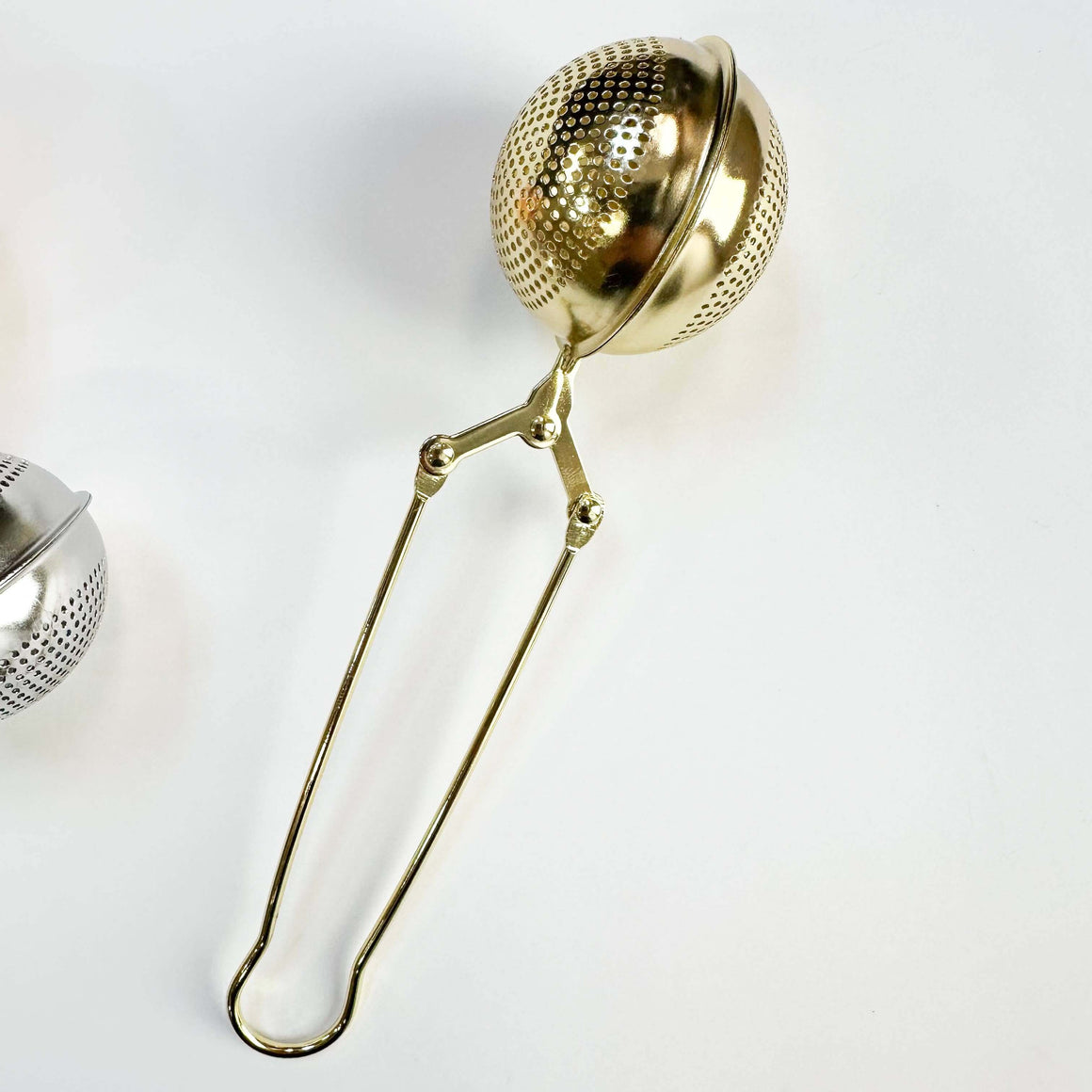 Gold metal tea infuser on a white background